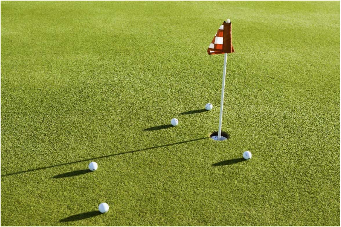 Golf balls on a putting green near the cup.